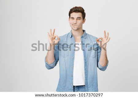 Portrait of cute boyfriend in denim with rolled sleeves showing okay gesture, isolated over white background. Barman got a request to make special drink and shows he understood.