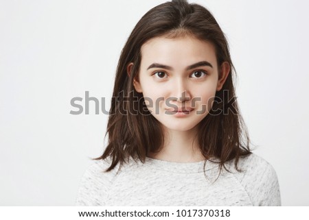 Portrait of cute naive european lop-eared girl with cute smile and mysterious look, over white background. Beautiful brunette makes photo for her profile in social network Royalty-Free Stock Photo #1017370318
