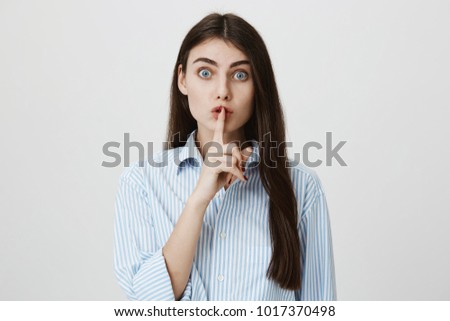 Indoor portrait of anxious-looking european female showing shh sign near mouth while staring at camera over gray background. Nanny give children some ice cream before lunch and wants keep it secret