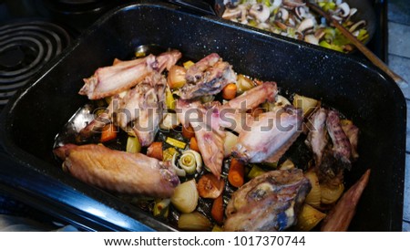 Pan of roasted turkey wings and mirepoix with mushrooms and leeks cooking at the back of the stove.
