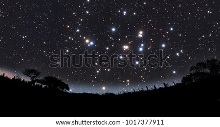 a composite arts of the universe with star cluster silhouetted with remote country side with hazy horizon
