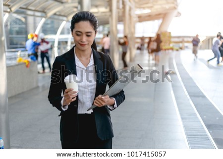 Business Woman holding a cup coffee and file Walking hastily on a city street.