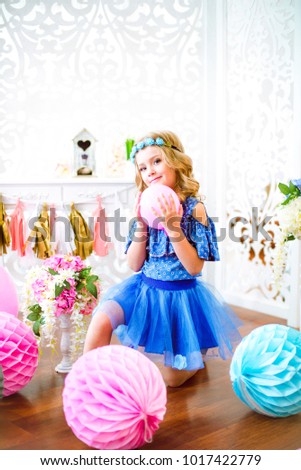 A portrait of a beautiful little girl laughs in a studio decorated many color balloons

