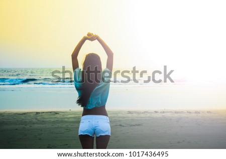 
Happy woman with raised up arms standing on near the sea at sunset