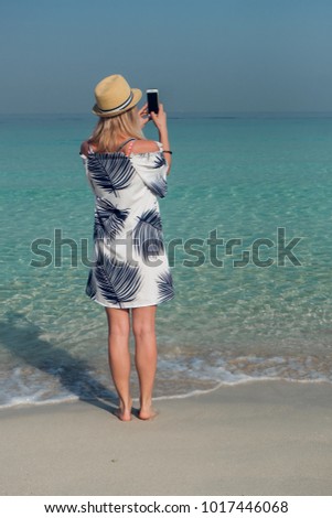 Young woman taking pictures of the ocean with a smart phone.