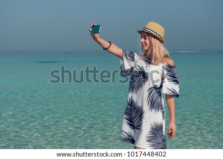 Young woman  taking a selfie with her phone in a tropical beach.