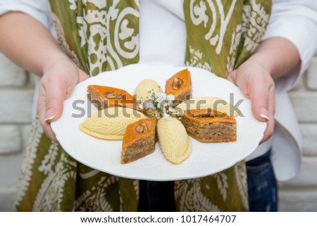 Woman in national kalagayi holding plate with shekerbura and pakhlava in hand