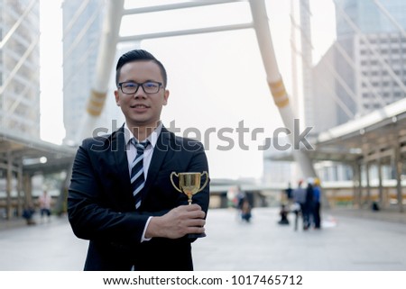 businessman, holding up a gold trophy cup is winner in a competition with city background. Win concept.