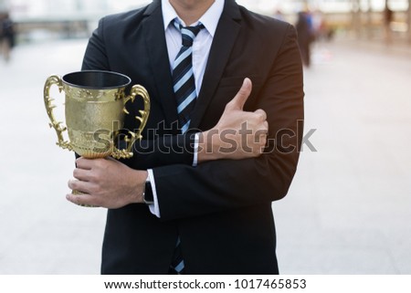 businessman, holding up a gold trophy cup is winner in a competition with city background. Win concept.