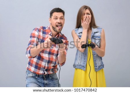Emotional couple with video game controllers on grey background