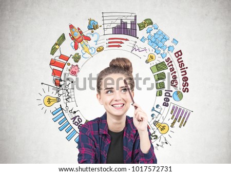 Smiling teen girl in a checkered shirt is sitting with a pencil near her forehead and thinking. She is looking up. A colorful round business plan sketch on a concrete wall.
