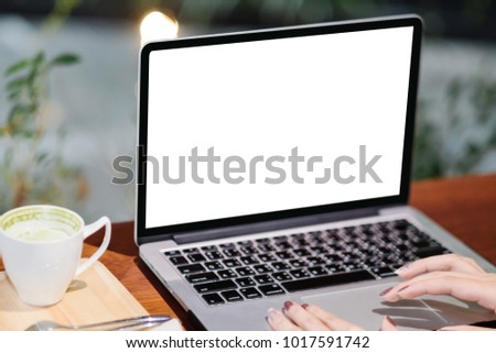 Mockup image of business woman using and typing on laptop with blank white screen and coffee cup on glass table in modern loft cafe, Soft focus on vintage wooden table.