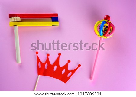 Purim Jewish celebration holiday greeting card. Crown red mask, colorful wooden noisemakers or graggers on pink background.Flat lay.Top view image, copy space.
