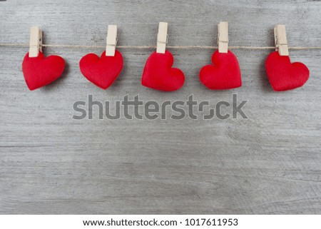 Five red heart hanging on a rope by a clamp on the old wooden board. Close up. 