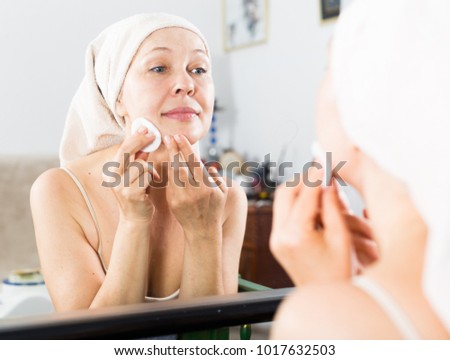 Elderly woman cleaning face for beauty procedures at home