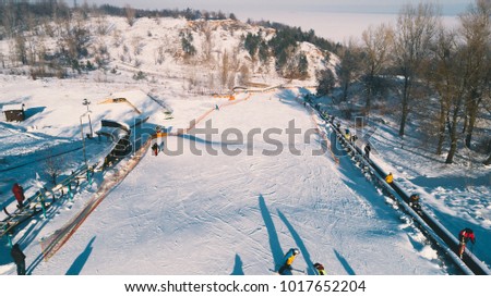 Aerial view of the descending mountain. Skiers and snowboarders descend from the mountain. People climb the escalator to the mountain. Trees. Winter. Snow. Ukraine. Vyshgorod. Vyshgora. Drone shot.