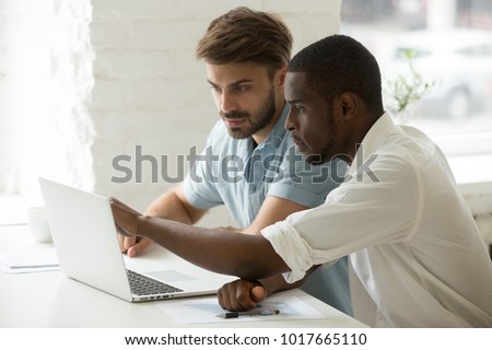 Multiracial team working together in office teamwork on laptop analyzing online business project result, focused serious african and caucasian businessmen looking at computer screen discussing data Royalty-Free Stock Photo #1017665110