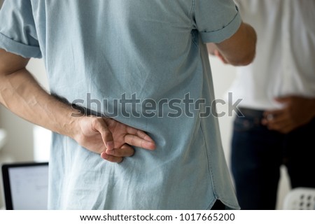 Dishonest caucasian businessman shaking hand of african partner holding crossed fingers behind back, sneaky hypocrite fake liar cheating friend, deception in business relations, close up rear view Royalty-Free Stock Photo #1017665200