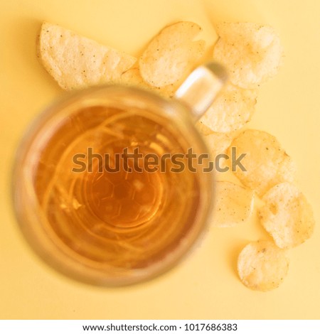 glass mug with beer and a picture of a soccer ball and chips on a yellow background. The view from the top.