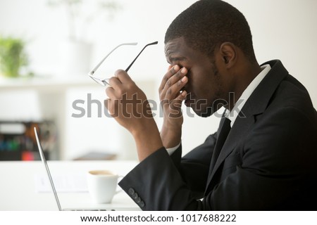 Tired of computer african businessman taking off glasses feels eye strain fatigue after long office work on laptop, exhausted overworked stressed depressed black man having bad sight vision problem Royalty-Free Stock Photo #1017688222