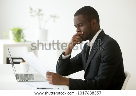 Serious african-american businessman employer thinking of business offer reading mail cover letter at workplace, puzzled black company executive looking at financial document considering contract Royalty-Free Stock Photo #1017688357