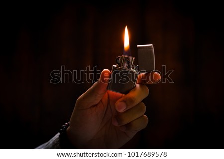 The man holding Brushed chrome lighter with windproof in the dark. Royalty-Free Stock Photo #1017689578