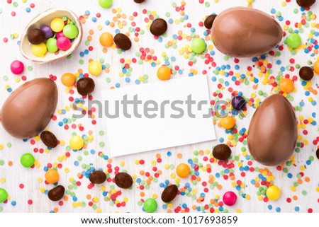 Easter chocolate egg with colorful candies. Sweet eggs on a white wooden background. Paper note