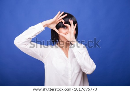 Woman makes a heart shape from her fingers on blue background in studio photo