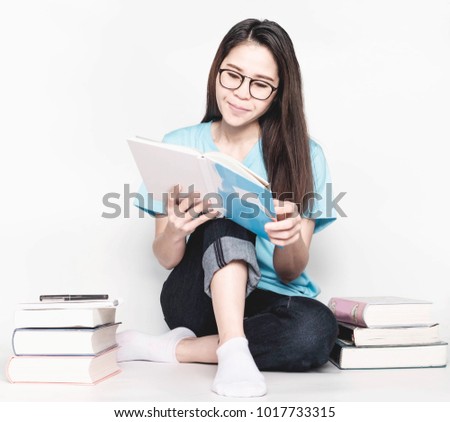 Asian girl Wearing blue t-shirts, glasses, reading books And a notebook with a pile of books and a cup of coffee on gray background