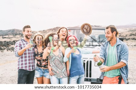 Group of happy friends making party in desert - Travel people having fun drinking champagne prosecco during their road trip with jeep car - Friendship, vacation, holidays lifestyle concept 