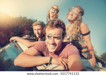 Group of happy people taking a selfie in a car at sunset in summer.