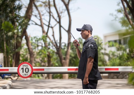 Asian Male Security Guard Talking a portable wireless transceiver in village  entrance . Security guard opening The entrance to the village door. Speed 10 limit in area,copy space.