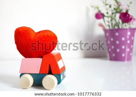 Wooden car carrying red heart for Valentines day with roses pot and white wall.