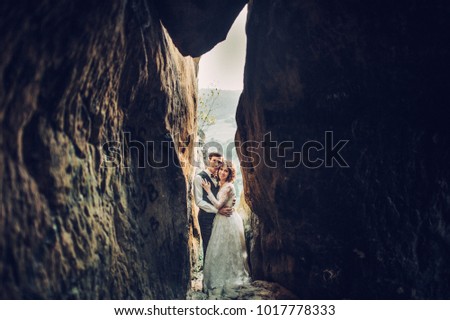 Young and romantic bride with her loving groom posing in darkened sandstone cleft