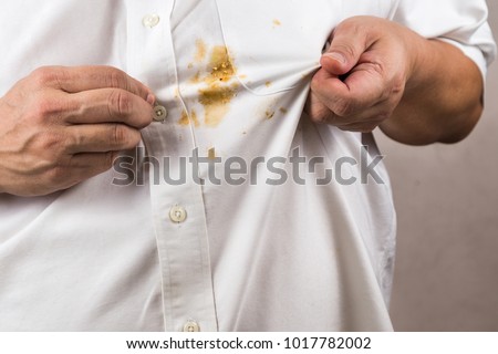 Frustrated person pointing to spilled curry stain on white shirt Royalty-Free Stock Photo #1017782002