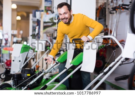 Smiling man tries to start a lawnmower in a garden tools store