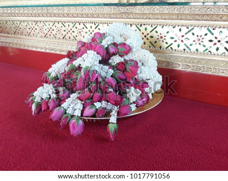 Jasmine garlands in a tray on red carpet in front of altar in the background