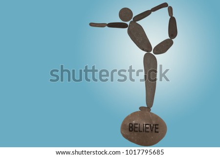 pebble art, pebbles, flat stones assembled made to resemble the human form, conceptual, the shape of a person doing yoga, standing bow balancing on a stone with the word believe carved in to it