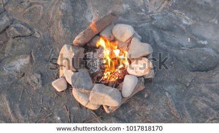 Bonfire burning on a rocky shore at dusk with rocks arranged in a circle 

