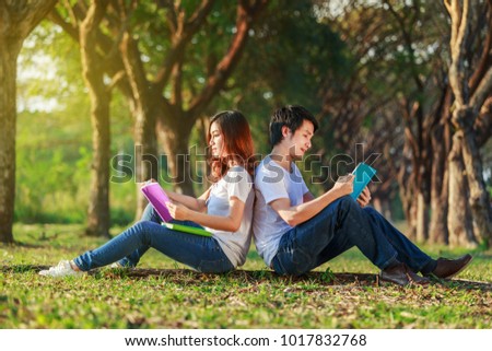 man and woman sitting and reading a book in the park