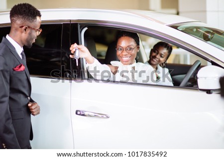 Young car african female salesman giving a key from the new car to the beautiful young african couple owners