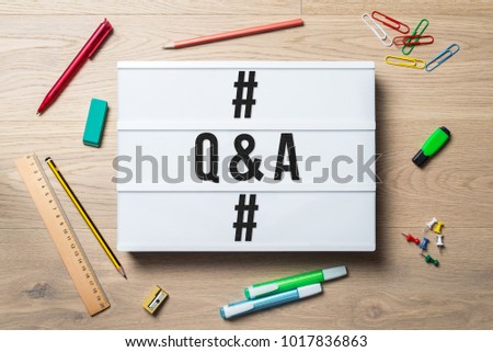 Q & A writing in hashtags in lightbox with pen, pencil, highlighter and ruler lying on office desk as flat lay