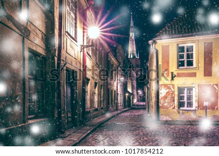 Narrow street illuminated of Medieval Old Town and St. Olaf Baptist Church at snowy winter night, Tallinn, Estonia