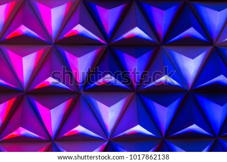 Design, background, texture concept. Close up of pyramids that made of cardboard and illuminated with the spotlights of such different bright coloures as pink, lilac and blue.