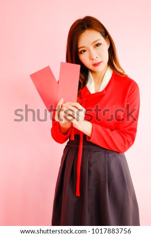 Portrait beautiful asian woman wearing red modern hanbok dress korea style on pink background with red envelopes holding in hand, celebrate chinese new year concept