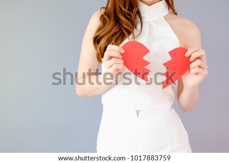 Portrait beautiful asian woman on gray background, unhappy in valentine day concept, model is holding red half heart in hand, broken-heart sign
