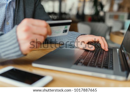 Cropped shot of a man's hands using a laptop at home while holding credit card in the hands, on-line shopping at home, cross process, filtered image