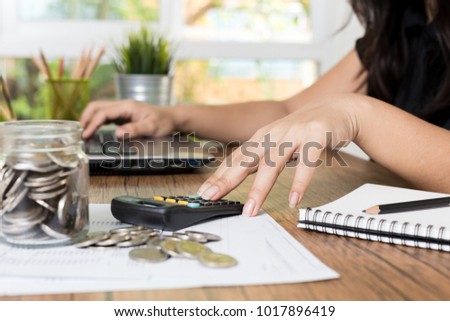 Saving money and finances concept, Close up hand woman hand put coins in jug glass with Calculate with a calculator. 
