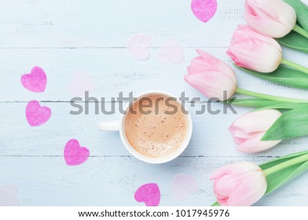 Spring tulip flowers and cup of coffee on pastel blue table top view. Beautiful spring breakfast on Mothers or Womans day. Flat lay.