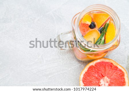 Glass jar of detox water with sliced grapefruit, blueberry and herbs and a fresh grapefruit on light concrete background, close up